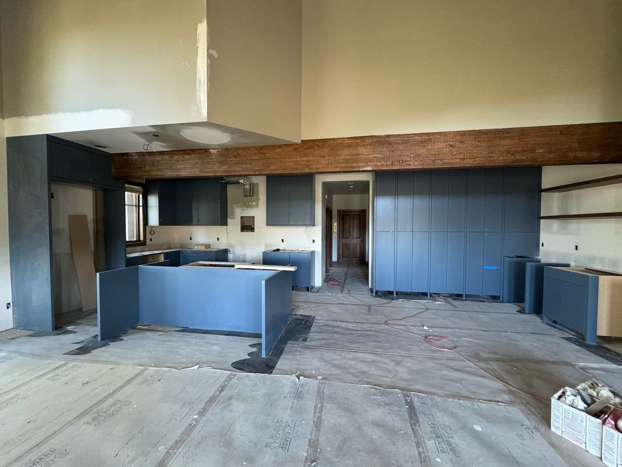 Slate-blue kitchen cabinets and island base set in place beneath the timber beam, counters not yet on